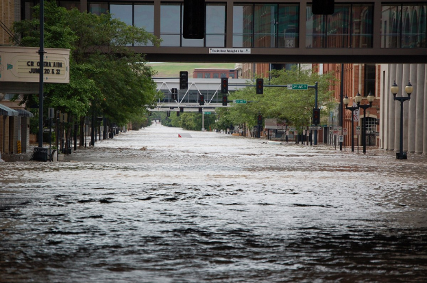 Stadtstraße überflutet mit Wasser, das die Straße, die Infrastruktur und Gebäude bedeckt, einschließlich einer Brücke im Hintergrund.