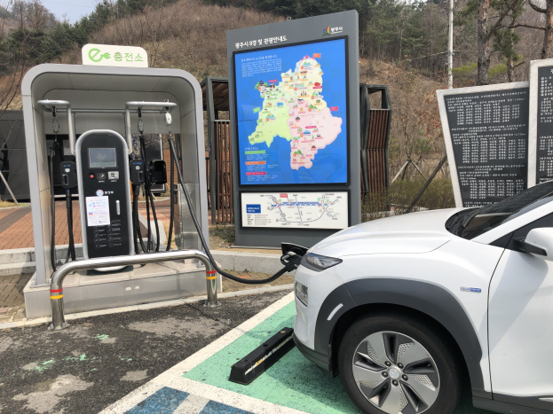 Ein Elektroauto lädt an einer Station in Seoul, Südkorea, mit Bäumen und Himmel im Hintergrund.