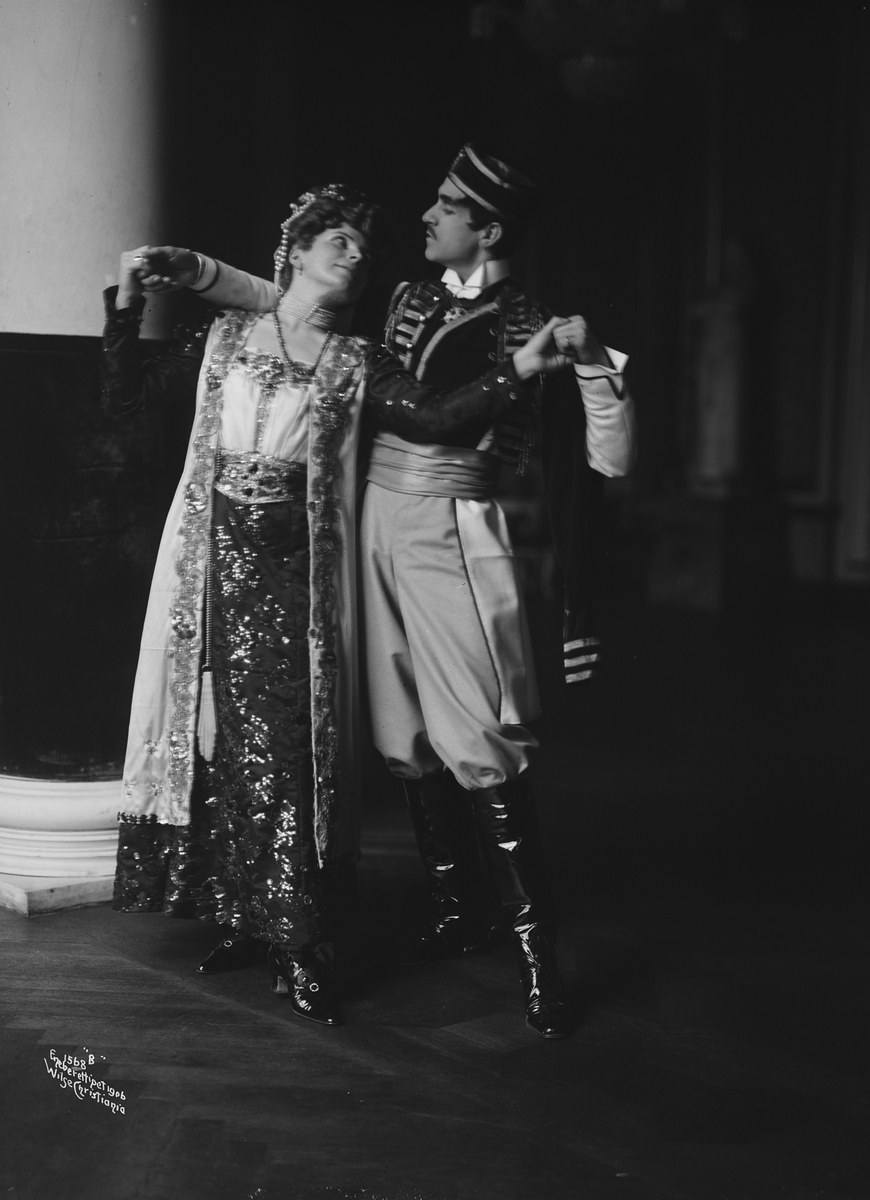 Schwarzes und weißes Foto eines Mannes und einer Frau, die in einem Ballsaal tanzen, mit einer Säule und einer Wand im Hintergrund; der Mann trägt Schuhe, was auf eine Vorstellung hinweist.