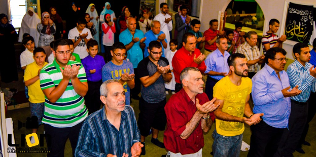 Menschen beten in einem Hall mit Text in der linken unteren Ecke.