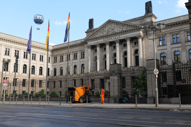 Großes modernes Gebäude mit vielen Fenstern, als Bundestag in Berlin, Deutschland identifiziert, umgeben von Straßeninfrastruktur und Fußgängern unter einem bewölkten Himmel.