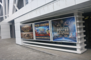 Großes Werbeplakat an der Seite eines Gebäudes für die Eröffnungszeremonie der Olympischen Spiele in Moskau, wobei das Gebäude auf der rechten Seite von Lichtern beleuchtet ist.