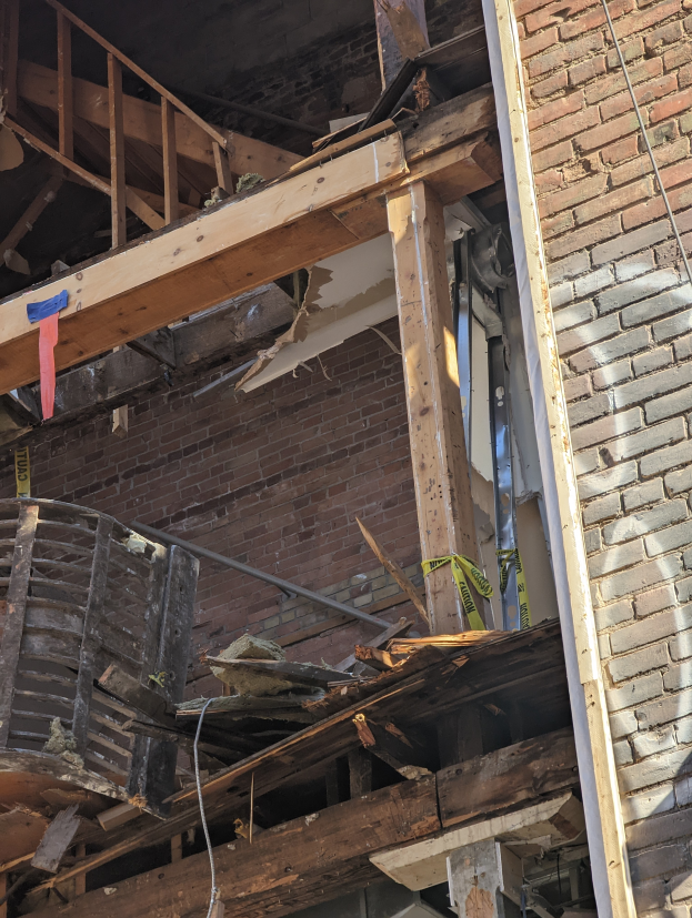 Teilweise abgerissenes Gebäude mit verstreuten Holzplanken und Trümmern, das gebrochene Fenster und Türen aufweist.