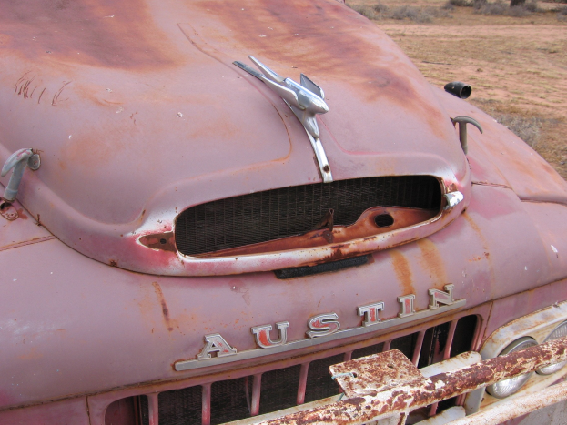 Alter rostiger Lastwagen auf einem Feld mit Bäumen und einem klaren blauen Himmel, der deutliche Rostschäden von langjähriger Witterungseinfluss zeigt.