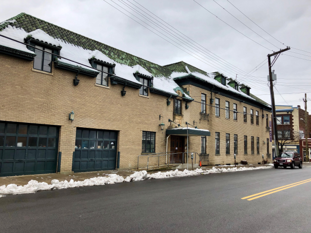 Großes Backsteingebäude mit einem grünen Dach an einer Straßenkreuzung, beschriftet als ehemalige St. Louis-Feuerwache, umgeben von Fahrzeugen, Schnee, Strommasten, Bäumen und einem bewölkten Himmel.