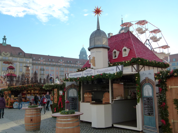 Ein geschäftiger Weihnachtsmarkt in Nürnberg, Deutschland, mit Menschen um dekorierte Stände, festlicher Beleuchtung, einem Riesenrad im Hintergrund und einer Tafel auf der rechten Seite.