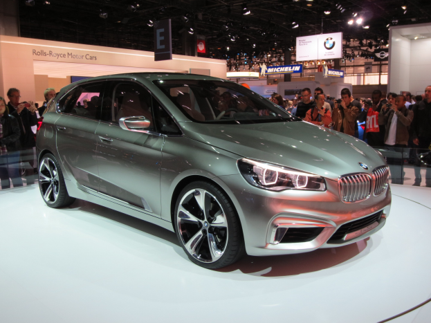 BMW 2er Active Tourer Concept auf der IAA in Frankfurt zu sehen, umgeben von Menschen, die Fotos machen, unter Deckenlampen mit Texttafeln im Hintergrund.