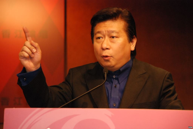 Ein Mann in Anzug und Krawatte, der vor einem Podium mit Mikrofon eine Rede hält und ernst dreinschaut.