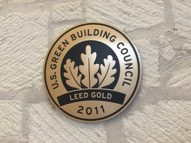 Logo der U.S. Green Building Council an einer Gebäudefassade, mit einem grünen Schild mit weißer Umrandung, schwarzer Schrift und einem umgebenden Lorbeerkranz.