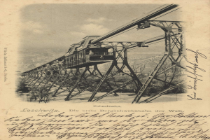 Ein altes Schwarz-Weiß-Foto einer Eisenbahnbrücke mit einem Kran, umgeben von Bäumen und einem bewölkten Himmel, mit dem Text "Bahnstrecka, die erste Eisenbahnbrücke Deutschlands" unten.