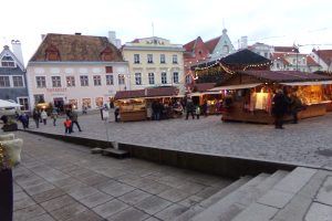 Ein geschäftiges Weihnachtsmarkt in Tallinn, Estland mit Menschen um geschmückte Stände, festliche Lichter, bewölkten Himmel, Treppe nach oben und Topfpflanzen im Bereich.