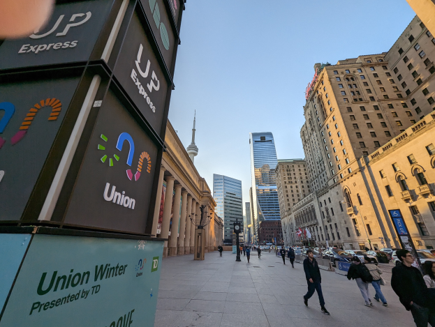Eine belebte Stadtstraße mit Fußgängern, hohen Gebäuden, Fahrzeugen und Schildern im Zusammenhang mit der Union Winter Conference, unter einem sichtbaren Himmel.