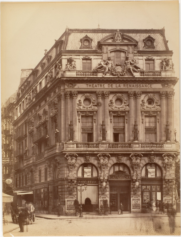 Schwarz-weißes Foto des Théâtre de la Renaissance in Paris mit einer Fassade mit Fenstern, Säulen, Bögen und Skulpturen sowie einigen Menschen und Fahrzeugen davor und dem Himmel im Hintergrund.