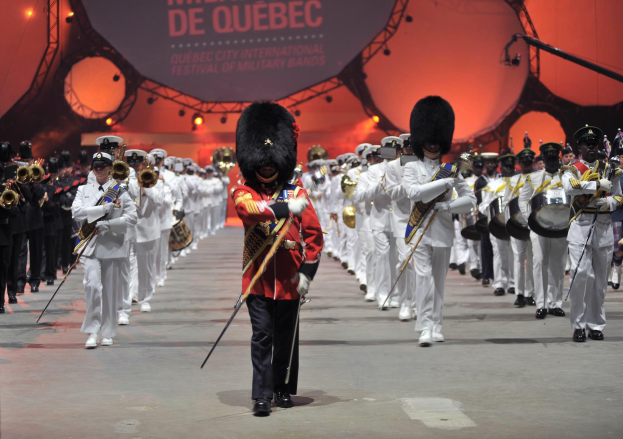 Eine Gruppe von uniformierten Menschen marschiert auf einer Straße, einige spielen Musikinstrumente, während der Eröffnungszeremonie des Montreal International Festival of Military Bands.