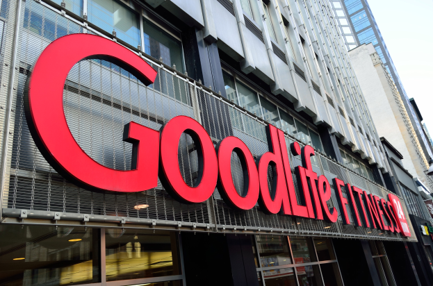 Ein Goodlife Fitness-Studio in New York City mit Glaswänden und einem Namen auf dem Gebäude, mit anderen Gebäuden auf der rechten Seite und dem Himmel im Hintergrund.