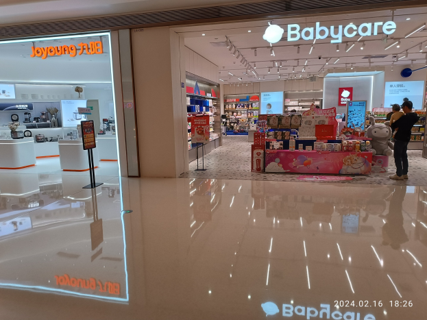 Babybedarfsladen im Mall of Asia, mit Menschen umgeben von Spielzeugen, Regalen, Schildern und einem Bildschirm unter Deckenleuchten.
