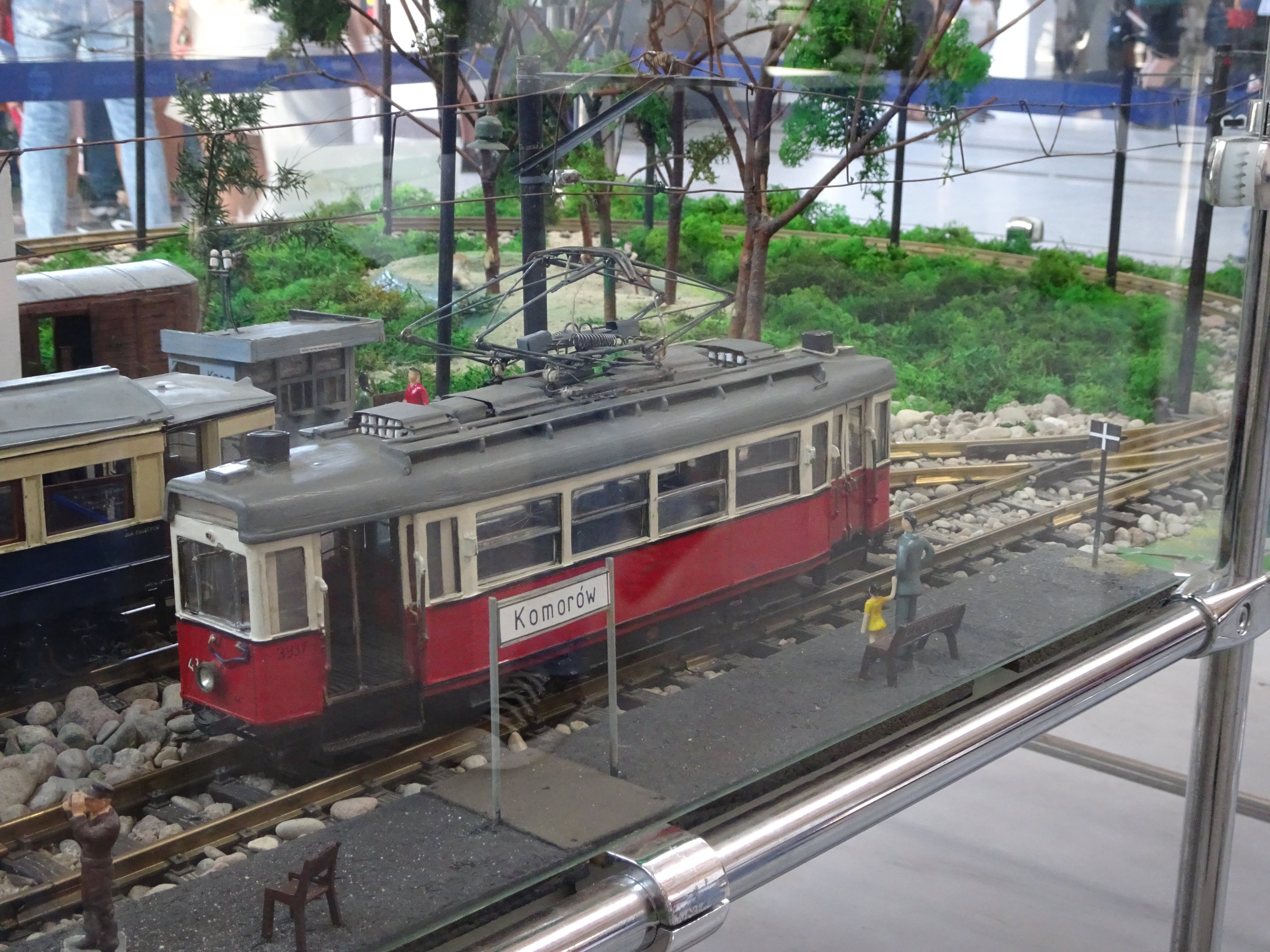 Modellbahnausstellung in einer Glasvitrine mit Miniatur-Eisenbahnlandschaft und Zuschauern.