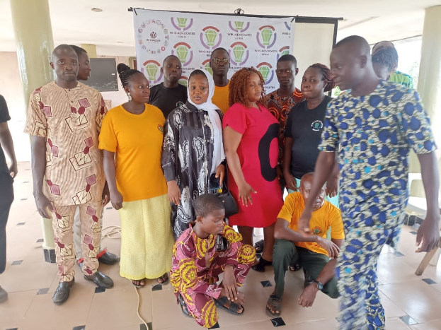 Eine Gruppe von Menschen vor einem Banner mit der Aufschrift "Advocates in Ghana: Ein Schritt-für-Schritt-Führer", umgeben von Stühlen, Säulen, einem Fernseher und einer Decke mit Deckenleuchten.