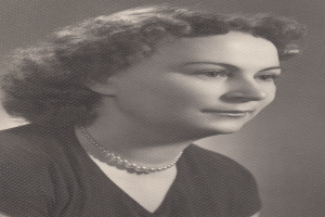 Ein Schwarz-Weiß-Foto einer Frau mit ernstem Gesichtsausdruck, deren Haare zurückgebunden sind und die eine Kette und ein einfaches Kleid mit hohem Kragen und langen Ärmeln trägt.