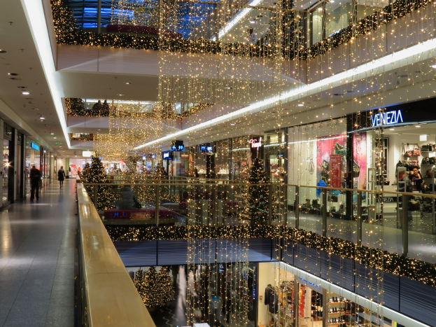 Das Innere eines Einkaufszentrums, geschmückt mit Weihnachtslichtern, mit Menschen, die herumlaufen, Geschäften mit Schildern, Glasgeländern und Lichtern, die von der Decke hängen, und einer festlichen und einladenden Atmosphäre.