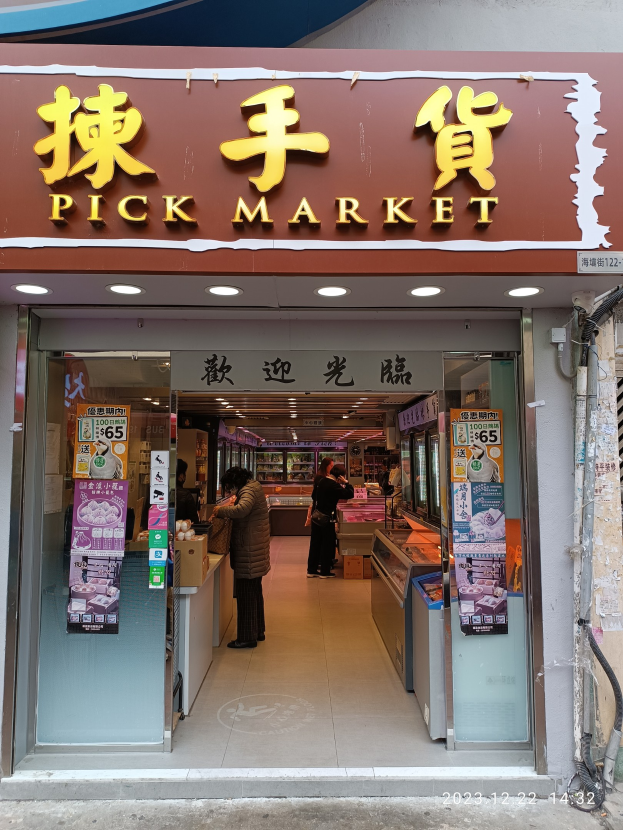 Ein belebter Hongkonger Straßenmarkt mit Händlern und einigen Menschen, mit einer Wand mit freiliegenden Rohren auf der rechten Seite.