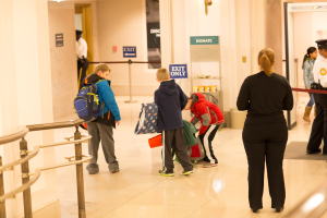 Gruppe von Menschen in einem Flur mit einem Geländer auf der linken Seite, Deckenleuchten und Informationsschildern im Hintergrund, die den ersten Schultag im U.S. Capitol anzeigen.