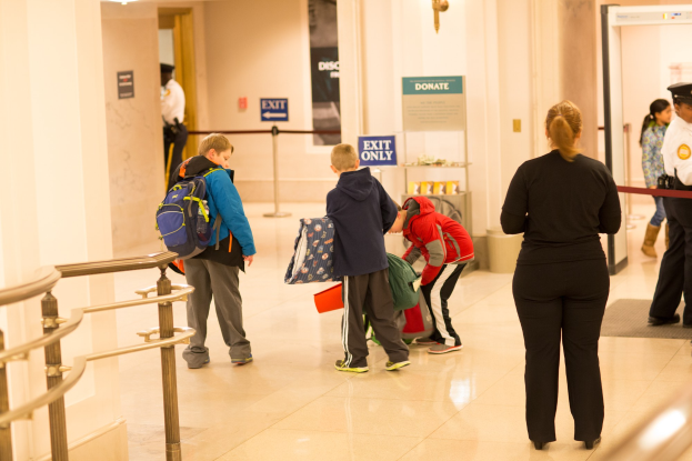 Gruppe von Menschen in einem Flur mit einem Geländer auf der linken Seite, Deckenleuchten und Informationsschildern im Hintergrund, die den ersten Schultag im U.S. Capitol anzeigen.