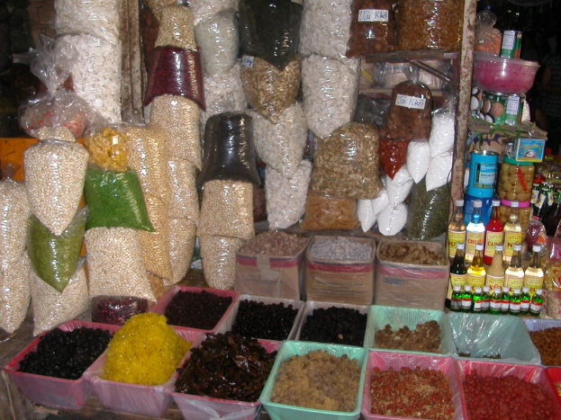 Ein Marktstand mit verschiedenen Lebensmitteln wie Flaschen und Schachteln, mit ein paar Menschen im Hintergrund.