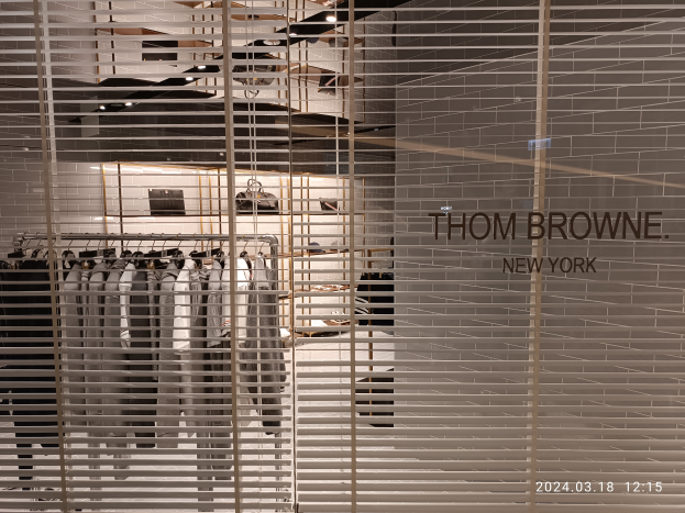 Ein Thomas Browne New York Flagship-Store-Innenraum mit Kleidung an Bügeln, Wandtext, Deckenleuchten und verschiedenen Gegenständen.