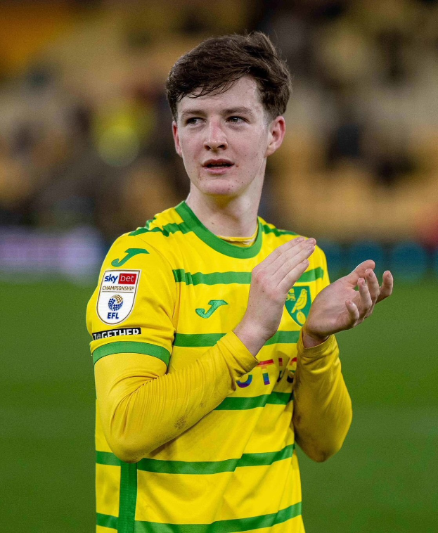 Ein junger Mann in einem gelb-grünen T-Shirt klatscht auf einem Fußballfeld, während er seine Torjubilierung feiert, mit einem unscharfen Hintergrund, der seine freudige Reaktion betont.