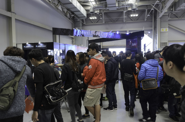 Eine Gruppe von Menschen vor einer Menge auf einer Gaming-Messe, mit Schildern, Lichtern und Rohren im Hintergrund.