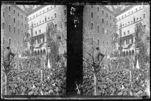Ein Schwarz-Weiß-Foto einer großen Menschenmenge vor einem Gebäude mit Fenstern, Bäumen und Flaggen im Hintergrund, die scheinbar eine Protestveranstaltung abhalten, wobei einige Schilder und Transparente halten.