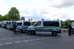Eine Gruppe von Polizeiwagen entlang einer Straße geparkt mit einem Radfahrer im Vordergrund und Gebäuden, Bäumen, Schildern im Hintergrund.