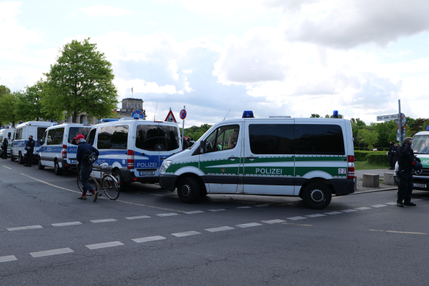 Eine Gruppe von Polizeiwagen entlang einer Straße geparkt mit einem Radfahrer im Vordergrund und Gebäuden, Bäumen, Schildern im Hintergrund.