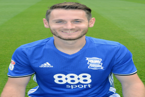 Ein Mann sitzt auf einem Fußballfeld in einem blauen T-Shirt, grinsend, mit Trainings-Session-Text unten.