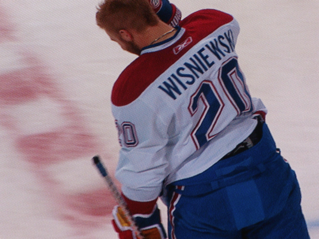 Ein konzentrierter Profi-Hockeyspieler in einem "Wisniewski"-Trikot steht auf dem Eis und hält einen Hockeystock.