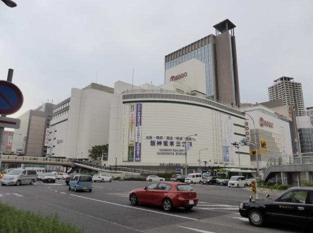 Eine belebte Stadtstraße mit Autos, hohen Gebäuden, Straßenmöbeln, Grünflächen und einem klaren Himmel, mit einem Konzertsaal mit einem Schild im Vordergrund.