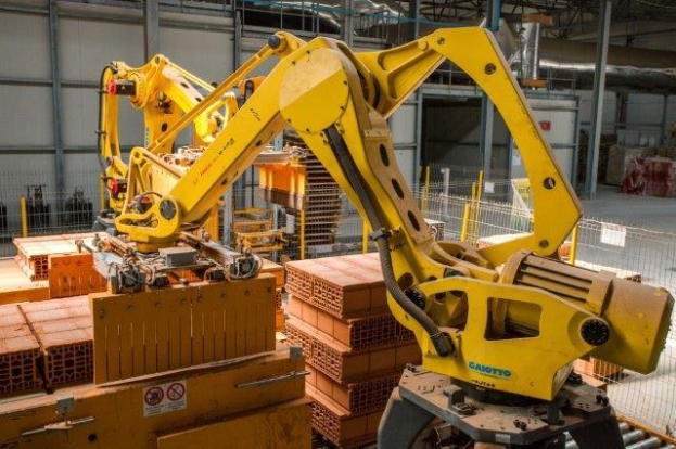 Großes Industriegebäude mit gestapelten Kisten, Kränen an der Decke, Zaun, Strommasten und einer fernen Wand in einer automatisierten Fertigungsanlage.