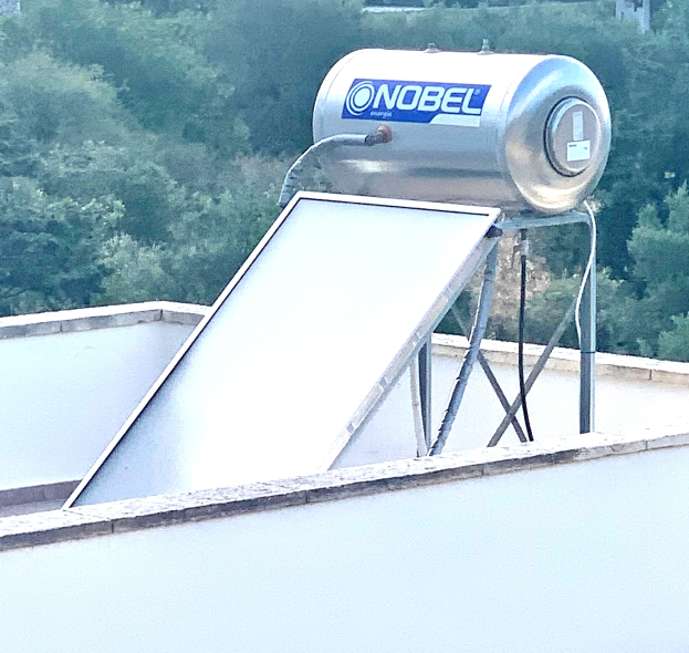 Solarwassererwärmer mit Speicherbehälter auf dem Dach eines Gebäudes montiert, Bäume im Hintergrund.