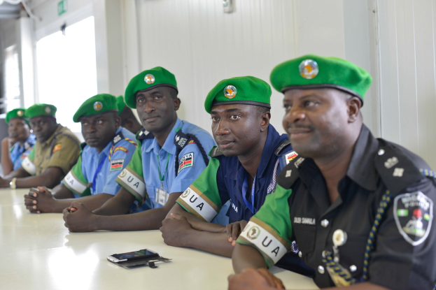 Eine Gruppe von Polizisten sitzt an einem Tisch während einer Schulung, mit Mobiltelefonen und anderen Gegenständen auf dem Tisch, in einem Raum mit Fenstern und Deckenbeleuchtung.