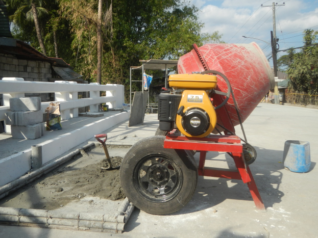 Betong-Mischer auf einem Zement-LKW umgeben von Baustoffen und einer Wohngegend unter einem bewölkten Himmel.