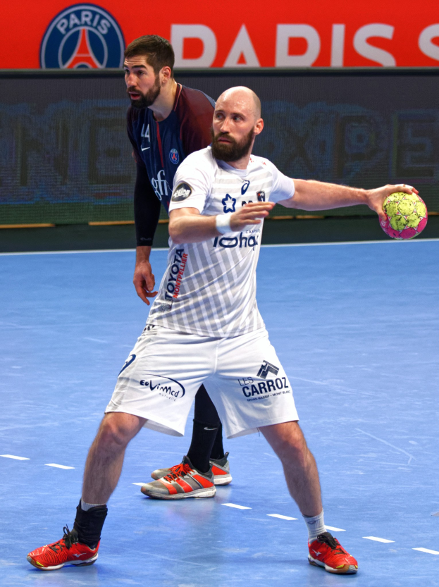 Zwei Männer spielen Handball auf einem Court, einer hält den Ball, mit einer Hintergrundtafel, die "Paris Saint-Germain vs Paris Saint-Germain" anzeigt.