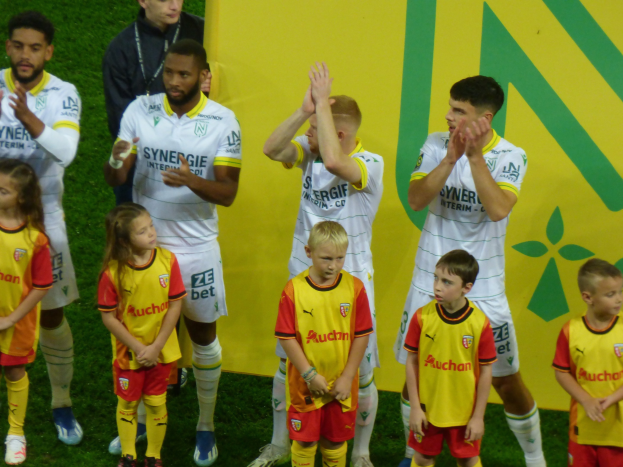 Gruppe von Fussballspielern in Uniformen, die auf einem Ligue 1-Feld klatschen und einen Sieg feiern.