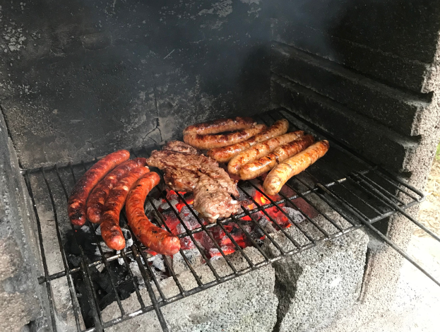 Grill mit Würstchen und Fleisch auf Kohle und Feuer, auf grüner Wiese im Freien.
