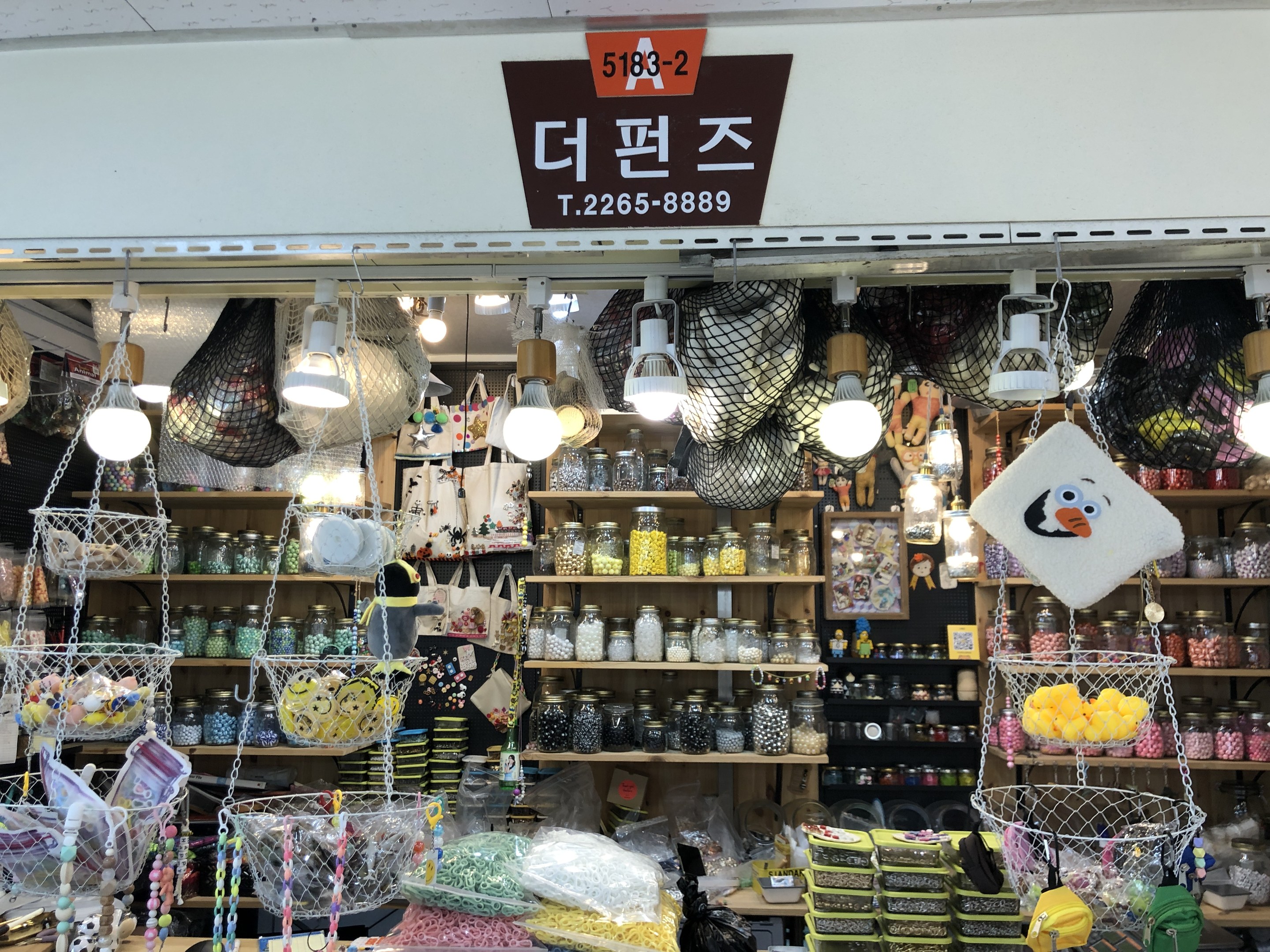 Ein unordentlicher Laden in Seoul, der verschiedene Gegenstände wie Körbe, Lampen, Flaschen und Spielzeuge auf Regalen ausstellt, mit einer Tafel oben, die anzeigt, dass es einer der besten koreanischen Läden ist.
