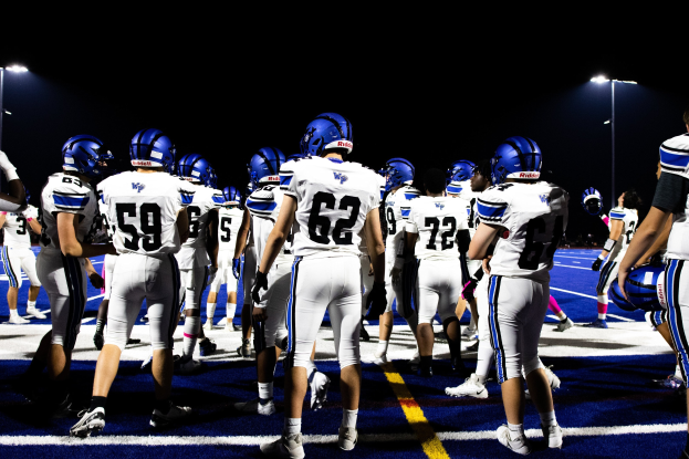 Eine Gruppe von Fußballspielern in Helmen und Stiefeln steht auf einem Feld unter Flutlichtmasten und sieht bereit für ein Spiel aus.