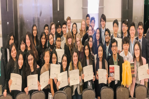 Gruppe von Menschen mit Urkunden in einem Raum mit Stühlen und einer Wand im Hintergrund, wahrscheinlich eine Abschlussfeier für das akademische Jahr 2019-2020.