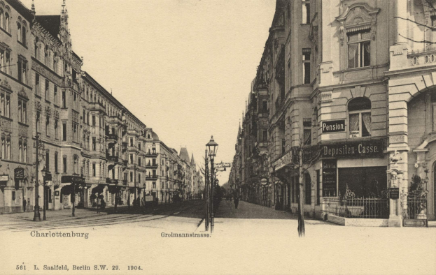 Altes Schwarz-Weiß-Foto einer Stadtstraße in Charlottenburg, Deutschland, mit Gebäuden, Straßenlaternen, Lampen, Namensschildern, Kraftfahrzeugen, Fußgängern, Gittern und einem klaren Himmel.