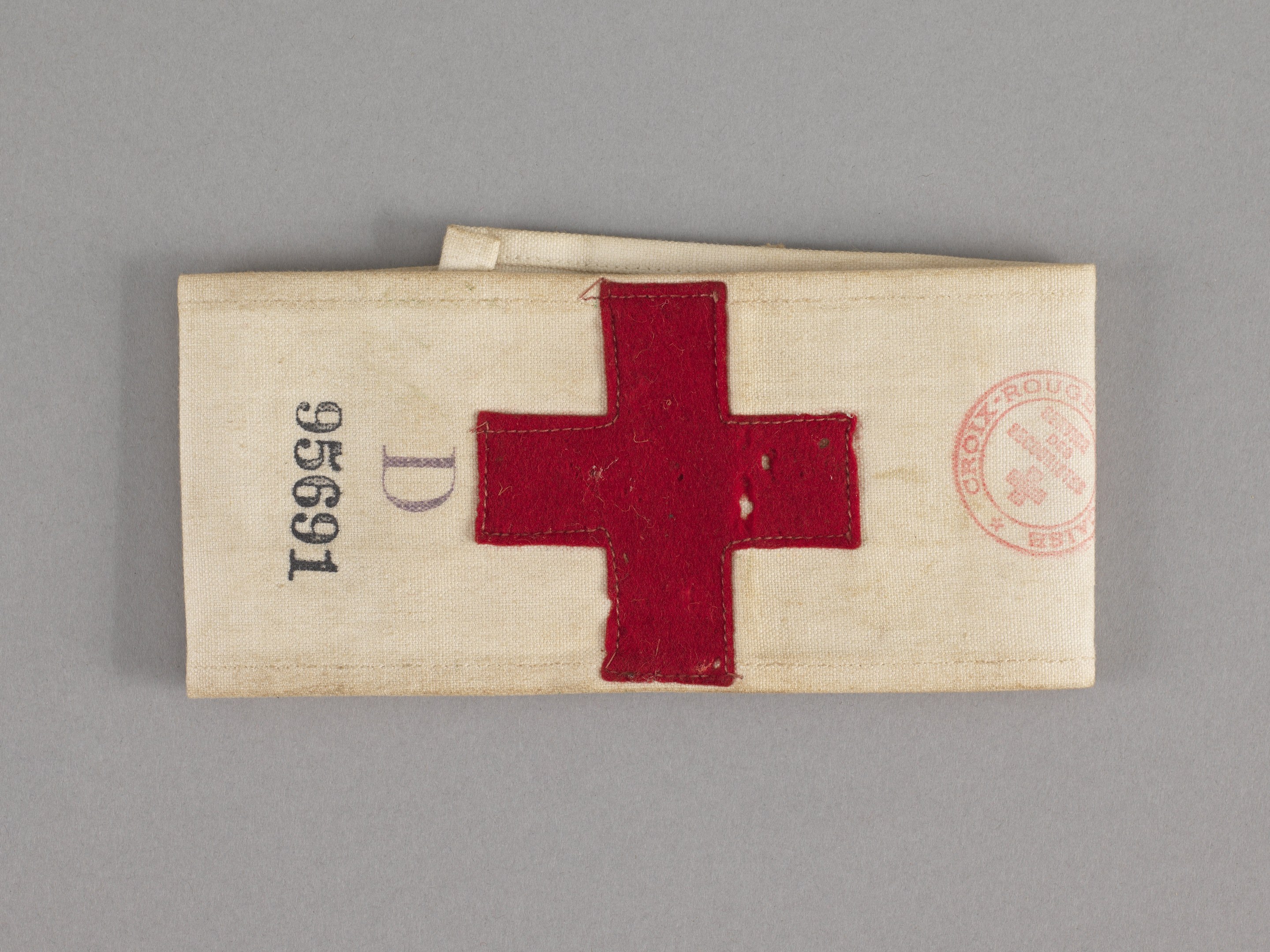 Ein rotes Kreuz-First-Aid-Kit in einer Stofftasche mit Text und einem Stempel, das auf einer Oberfläche liegt.