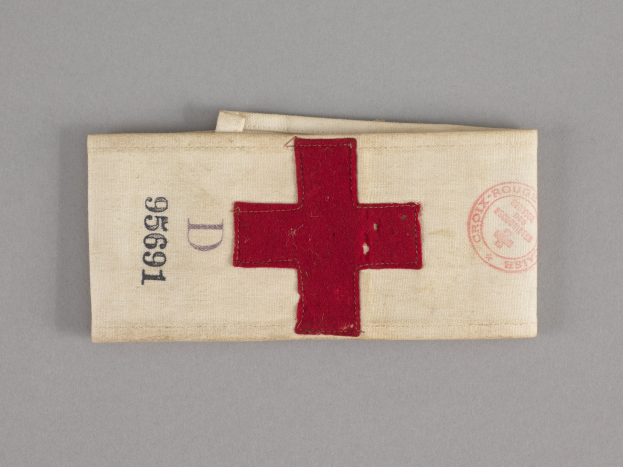 Ein rotes Kreuz-First-Aid-Kit in einer Stofftasche mit Text und einem Stempel, das auf einer Oberfläche liegt.